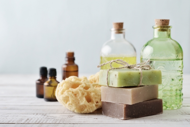 Stack of soap bars with sponge and bottles on light background
